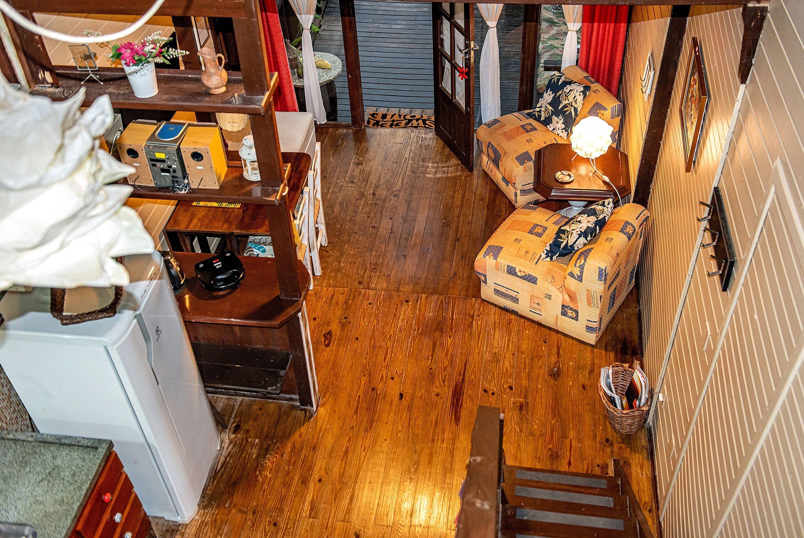 A compact living space with a wooden floor, a sofa, a small table with a lamp, and a refrigerator.
