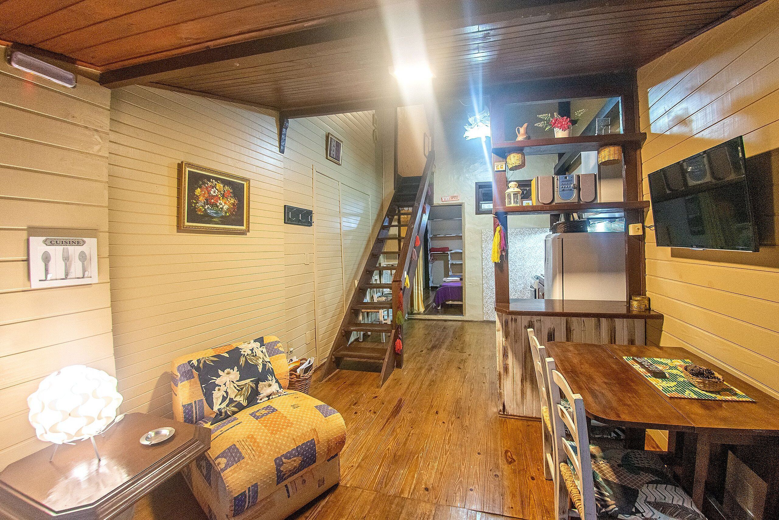 Ein gemütliches Interieur mit einer Holztreppe, einem Essbereich mit Tisch und Stühlen sowie einer Couch mit gemustertem Kissen.