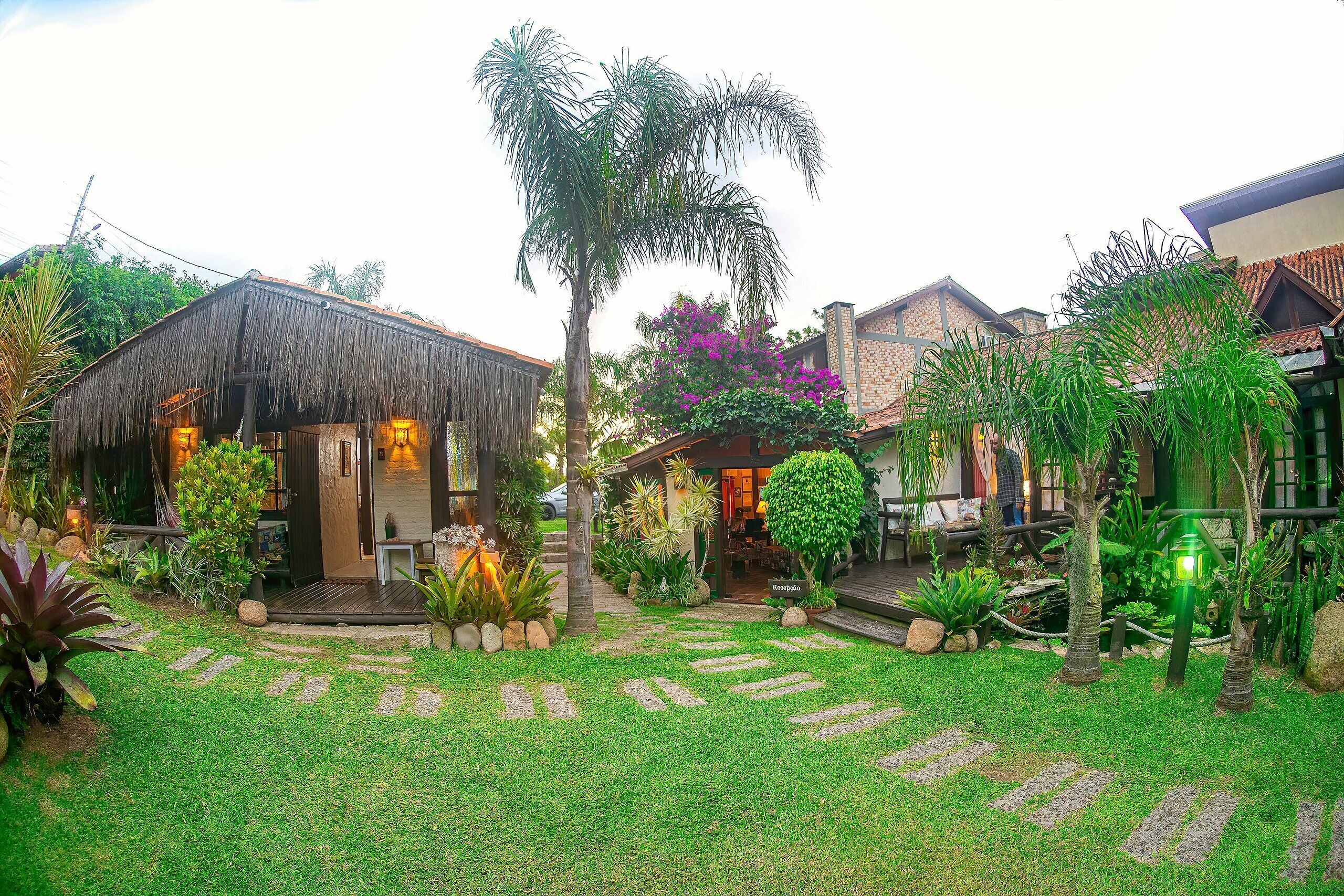 A well-maintained garden with a thatched-roof structure, stone pathway, and various tropical plants.