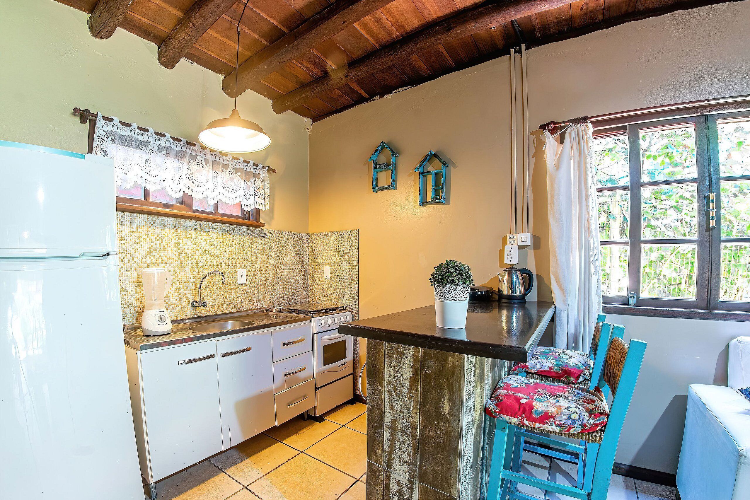 A kitchen with white cabinets, a stove, and a sink. There is a window with curtains and a view of greenery outside.