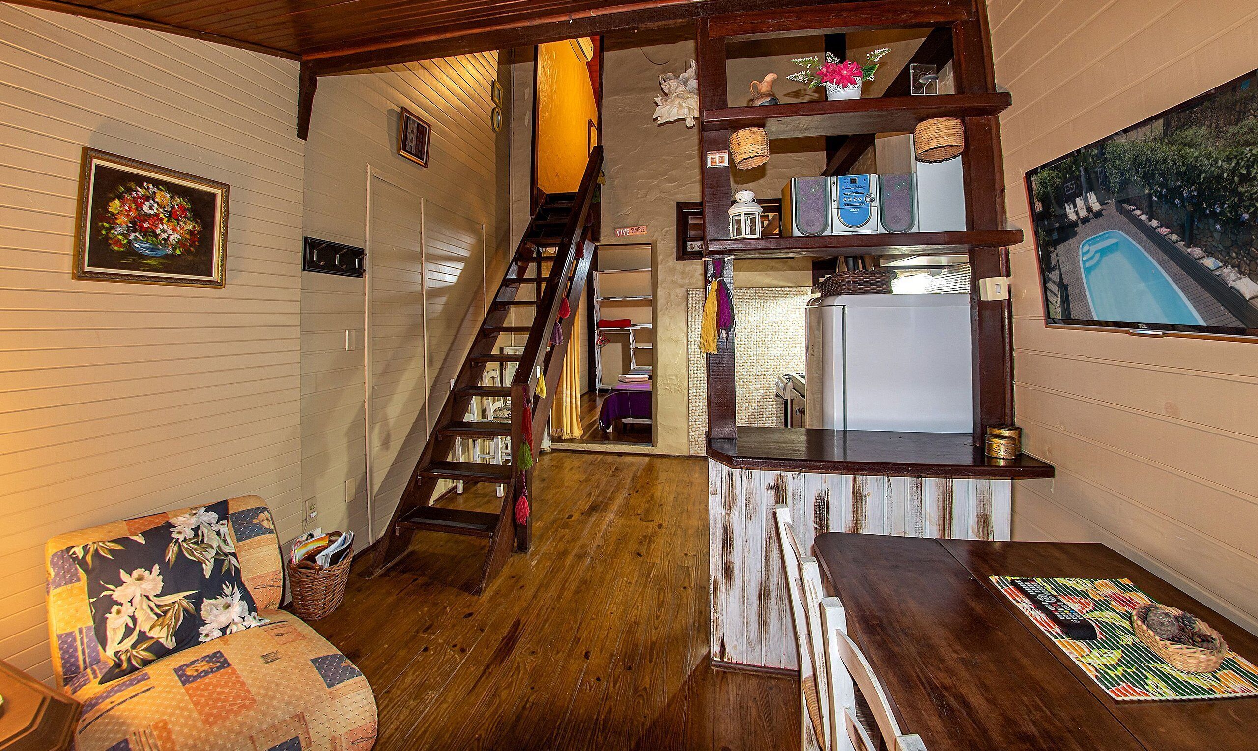 Un interior acogedor con una escalera de madera, un comedor y una cocina con refrigerador y televisor.