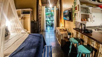 Un pasillo estrecho que conduce a un dormitorio con una cama, una mesita de noche con lámpara y una pequeña cocina equipada con taburetes y un fregadero.