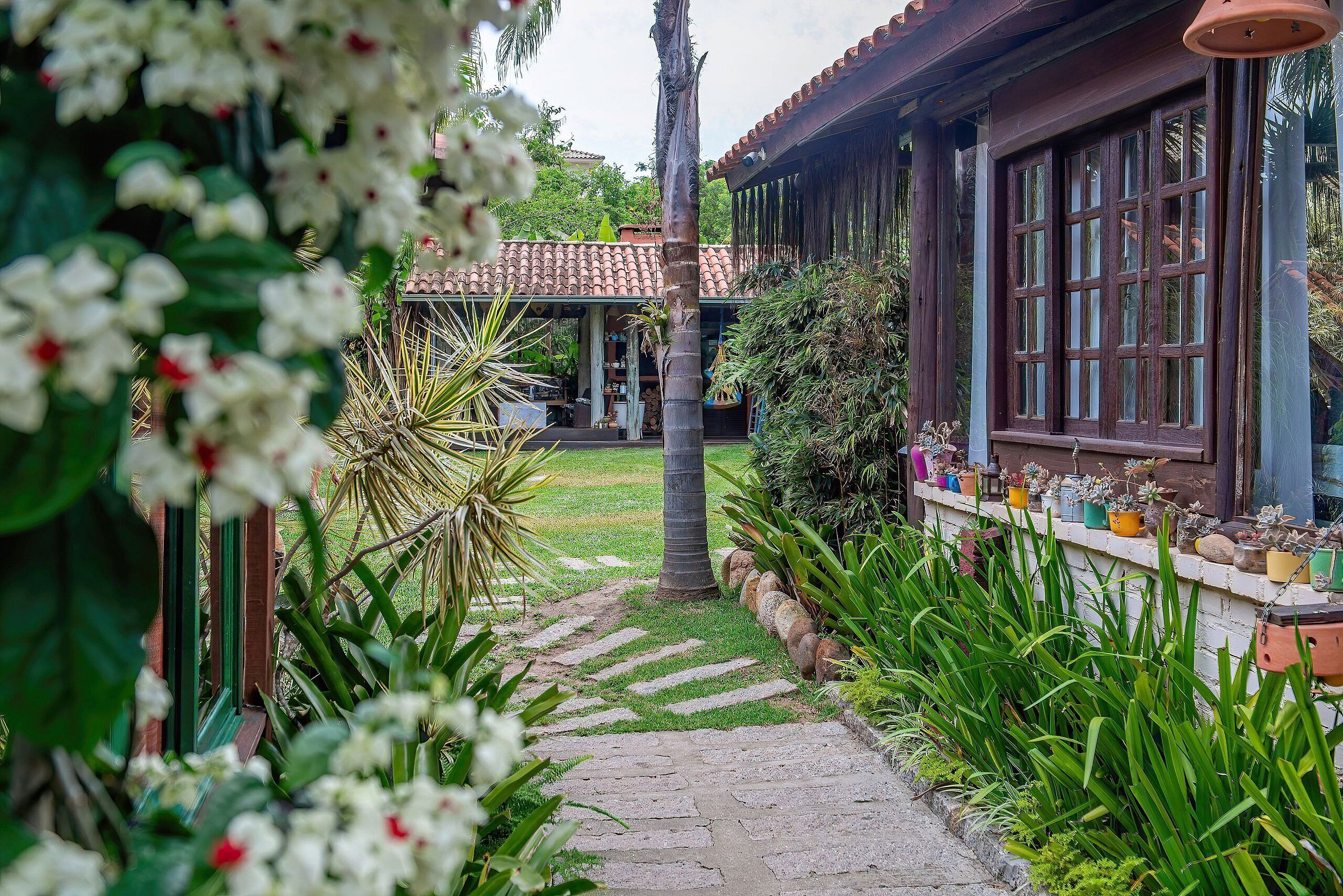 Un sendero en un jardín que conduce a un edificio con techo de tejas y ventanas grandes.