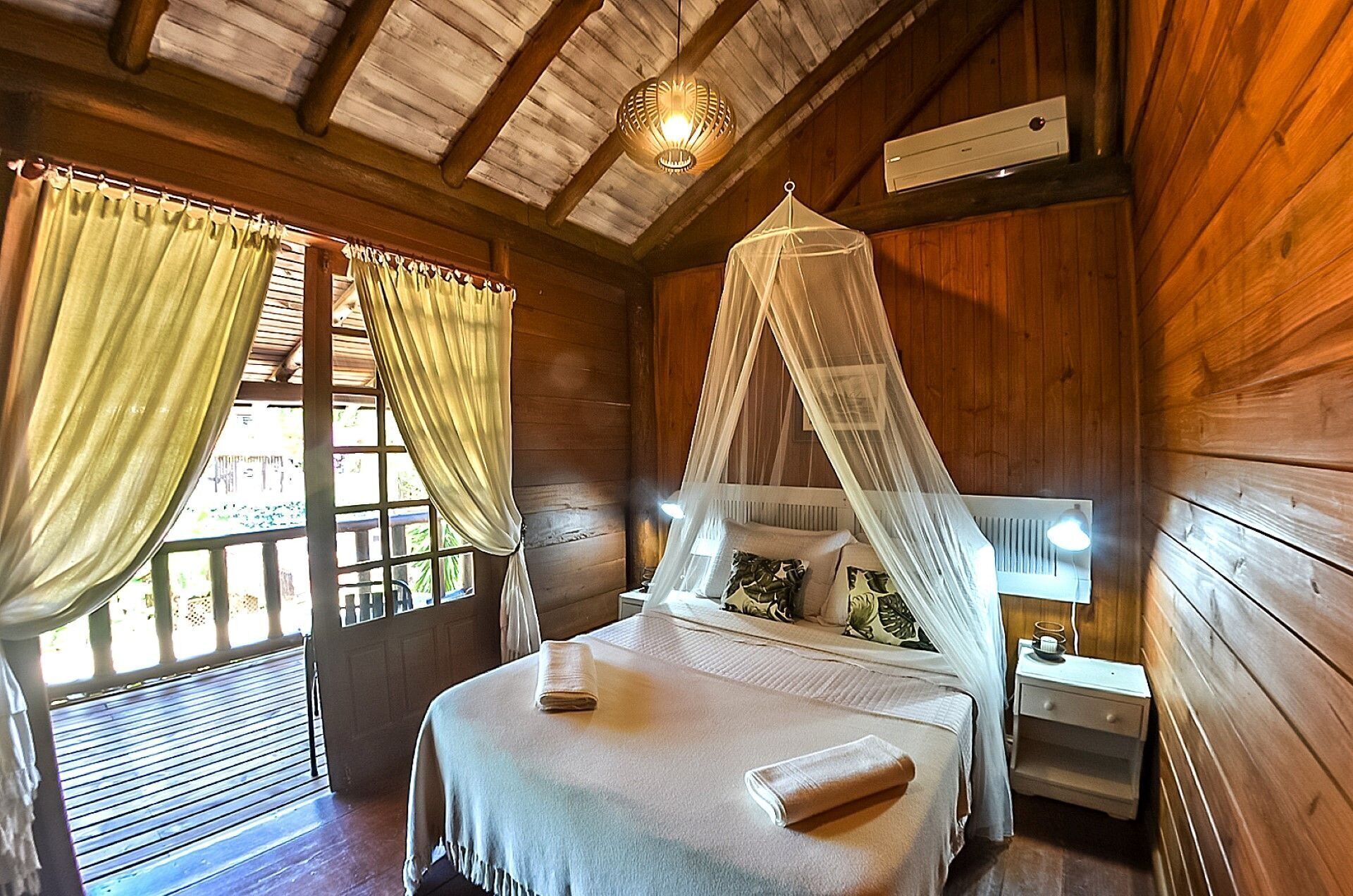 Una habitación de cabaña de madera con cama, mesita de noche, ventana con cortinas e iluminación en el techo.