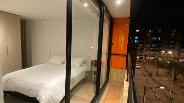 Un dormitorio con una cama grande, una silla y un ventanal que da a un balcón.