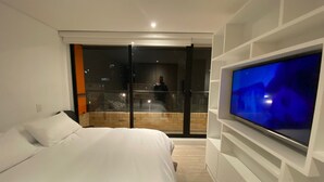 Un dormitorio moderno con una cama grande, un televisor montado en la pared y un balcón con puerta de vidrio.