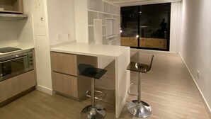 Una cocina moderna con una isla central, dos taburetes de bar y vista a la ciudad de noche a través de un amplio ventanal.