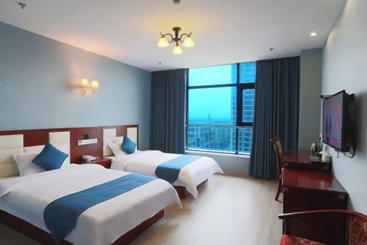 Une chambre d’hôtel avec deux lits, un bureau, une chaise, une télévision et une grande fenêtre avec des rideaux.