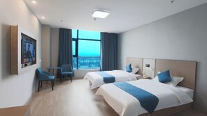 A hotel room with two beds, a desk, a chair, a window with curtains, and a mounted television.