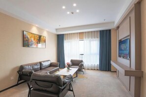 Une chambre d’hôtel moderne, dotée d’un canapé en cuir, d’une table basse, d’un téléviseur et d’une grande fenêtre avec des rideaux.