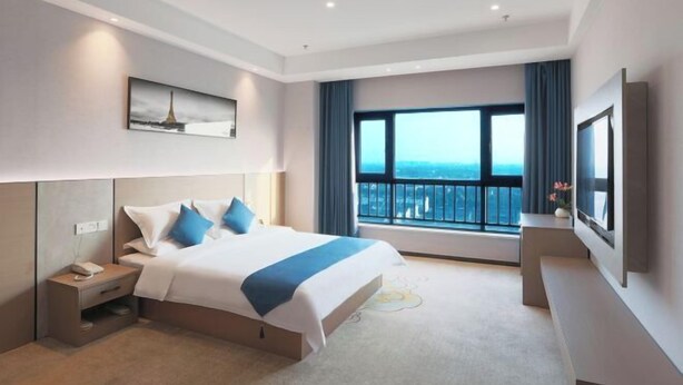 A modern hotel room with a large bed, a bedside table with a phone, a flat-screen TV, and a large window with a city view.
