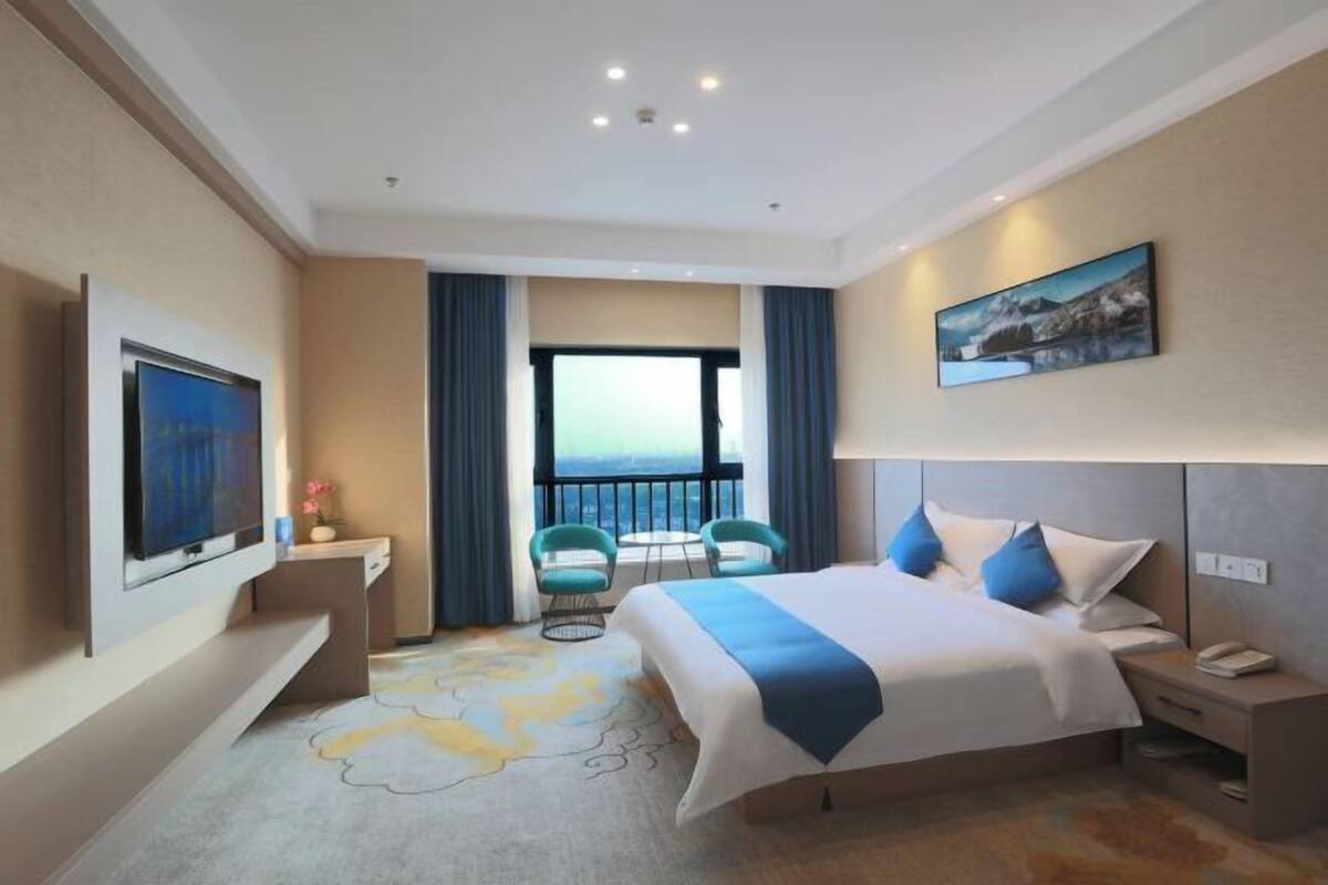 Une chambre d’hôtel avec un lit, une télévision, un bureau, une chaise, un balcon avec vue et un tableau au mur.