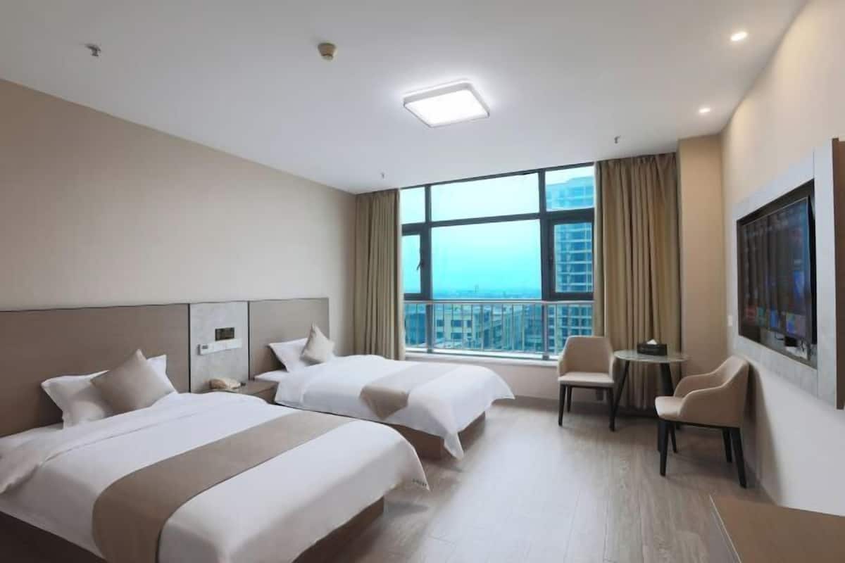 Une chambre d’hôtel avec deux lits, un bureau, une chaise, une fenêtre donnant sur la ville et un téléviseur à écran plat.