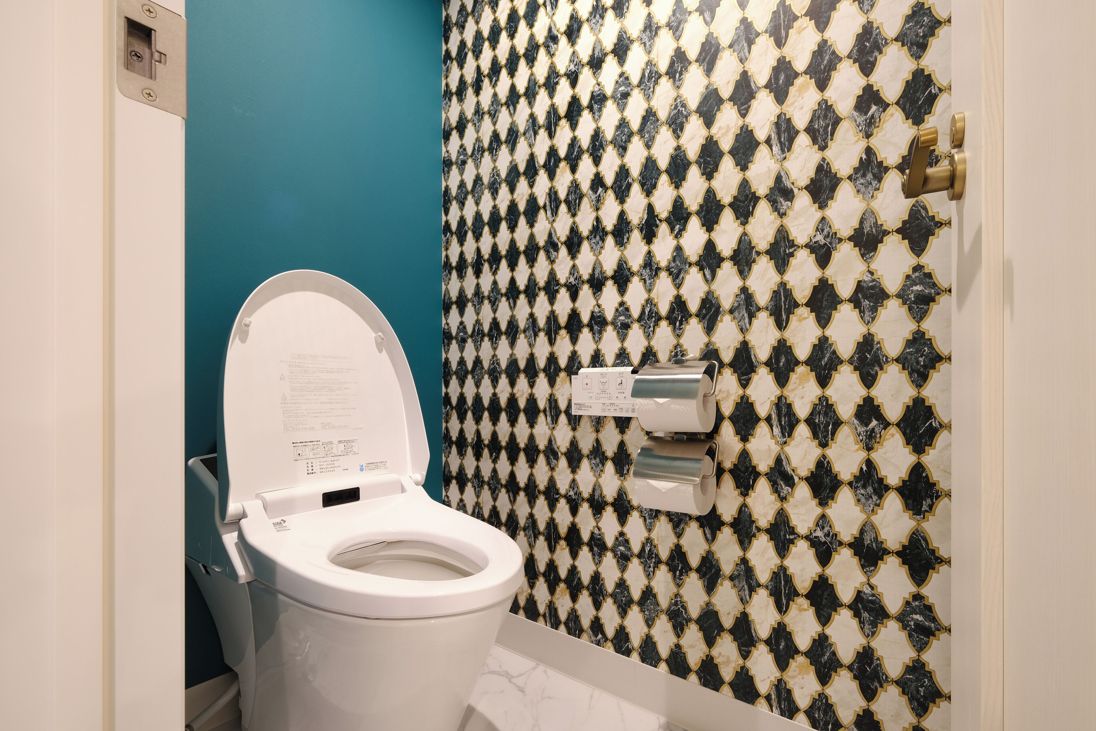 Un baño con inodoro, pared azul y un salpicadero de azulejos estampados.
