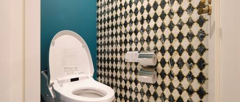 A bathroom with a toilet, a blue wall, and a patterned tile backsplash.