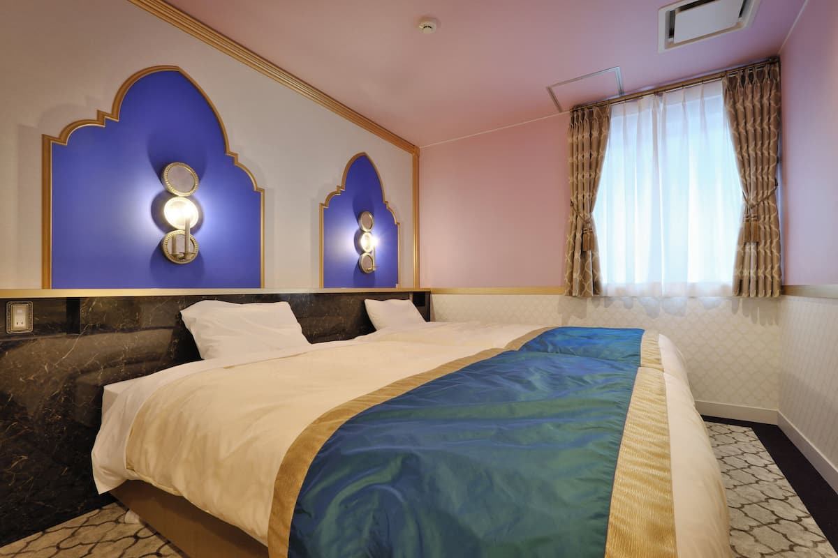 A hotel room with a large bed, two wall sconces, a window with curtains, and a patterned floor.