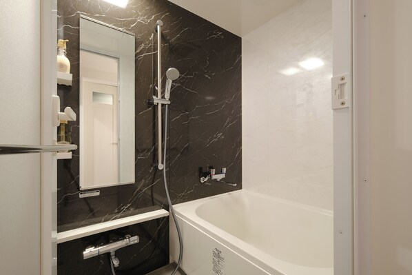 A modern bathroom with a large bathtub, a handheld showerhead, and a built-in mirror.