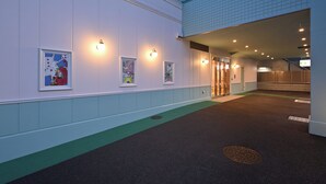 Entrada de hotel con un corredor cubierto, obras de arte enmarcadas y un área alfombrada de color verde.