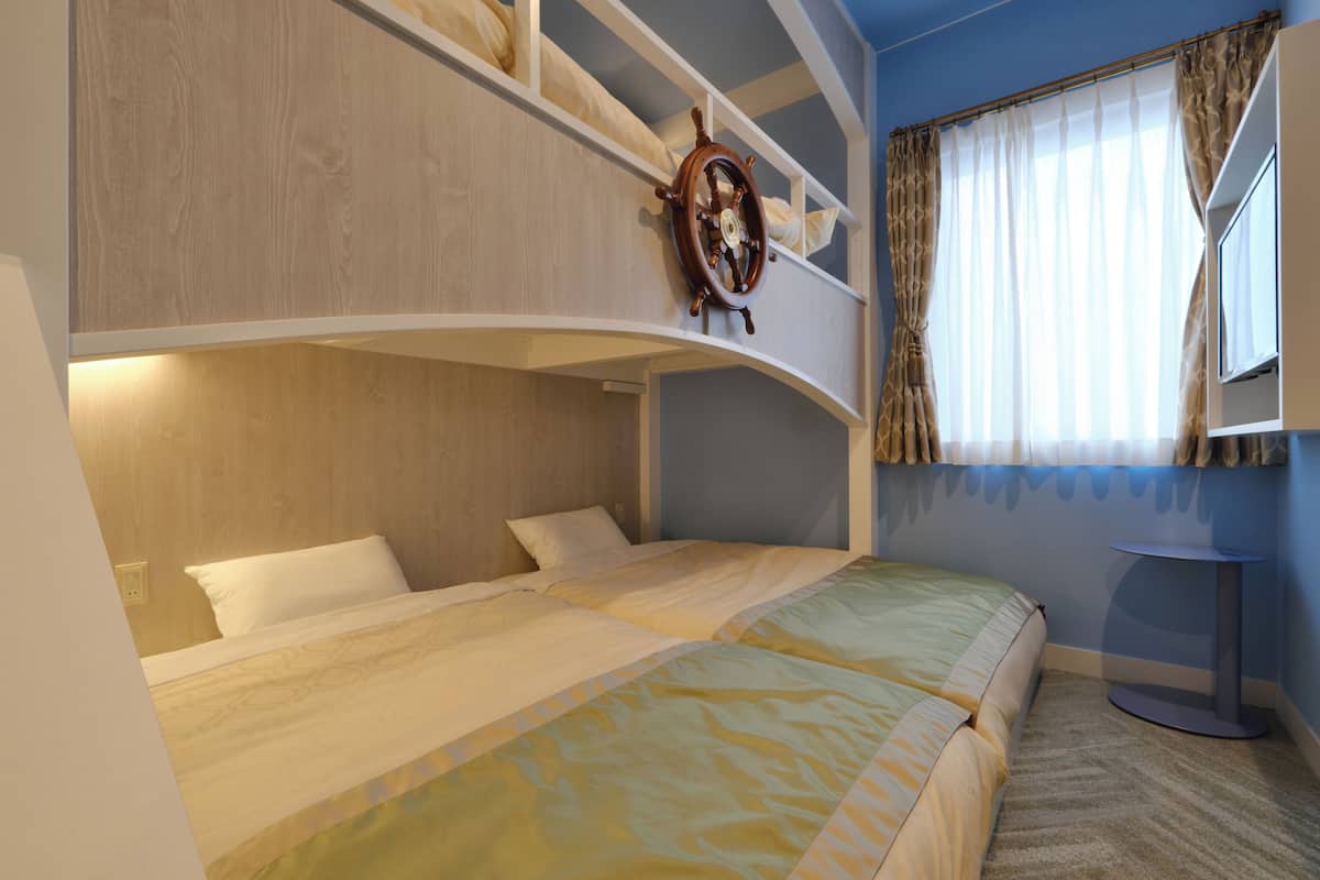 A bedroom with a bunk bed, a ship's wheel decoration, a bedside table, and a window with curtains.