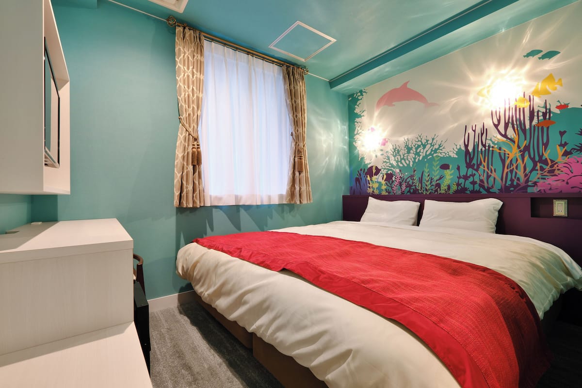 A bedroom with a bed, a window with curtains, a wall mural of an underwater scene, and a nightstand.