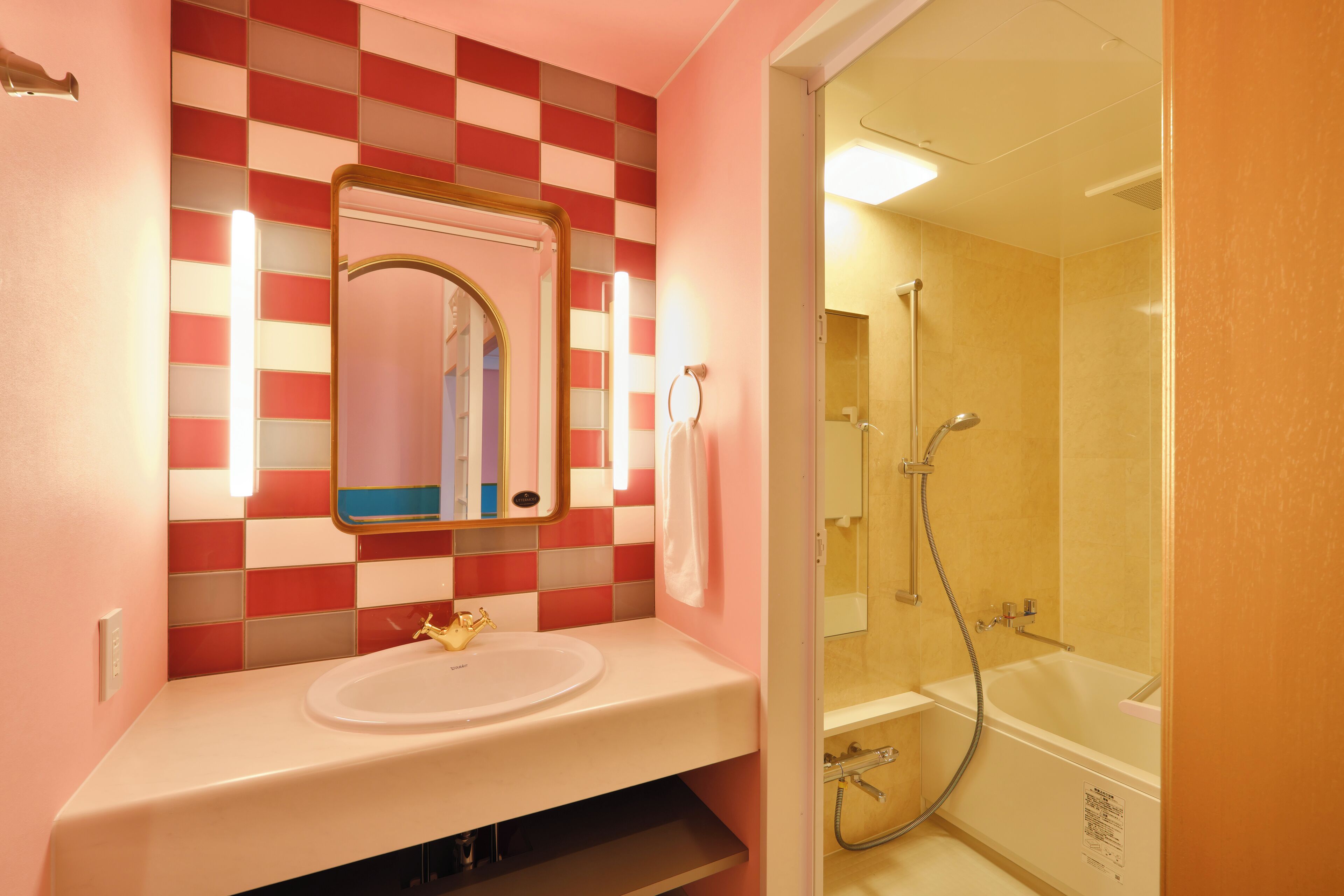 A bathroom with a pink and red checkered wall, a white sink, and a shower area.
