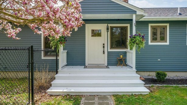 Ein Haus mit Veranda, einer weißen Tür und einem kleinen Garten.
