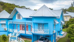Een blauw huis met een wit balkon, een rode deur en een auto ervoor geparkeerd.