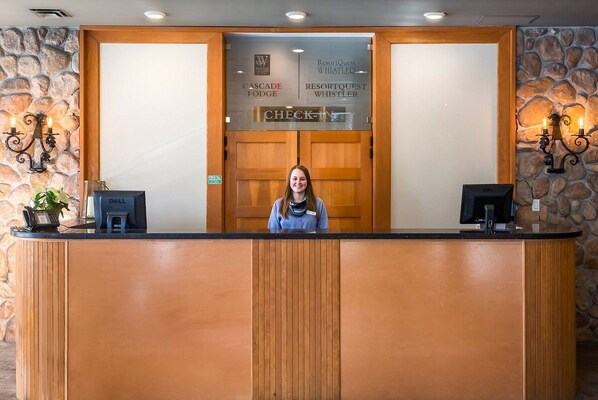 A reception desk with a receptionist, a check-in counter, and a stone wall. - Cascade Lodge - Studio Suite (Whistler)