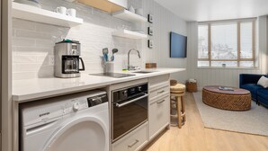 A modern kitchen with built-in appliances, a dining area with a round table, and a living room with a blue sofa. - Cascade Lodge - Studio Suite (Whistler)