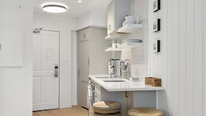 A modern kitchen with white cabinetry, a white countertop, and two stools. - Cascade Lodge - Studio Suite (Whistler)