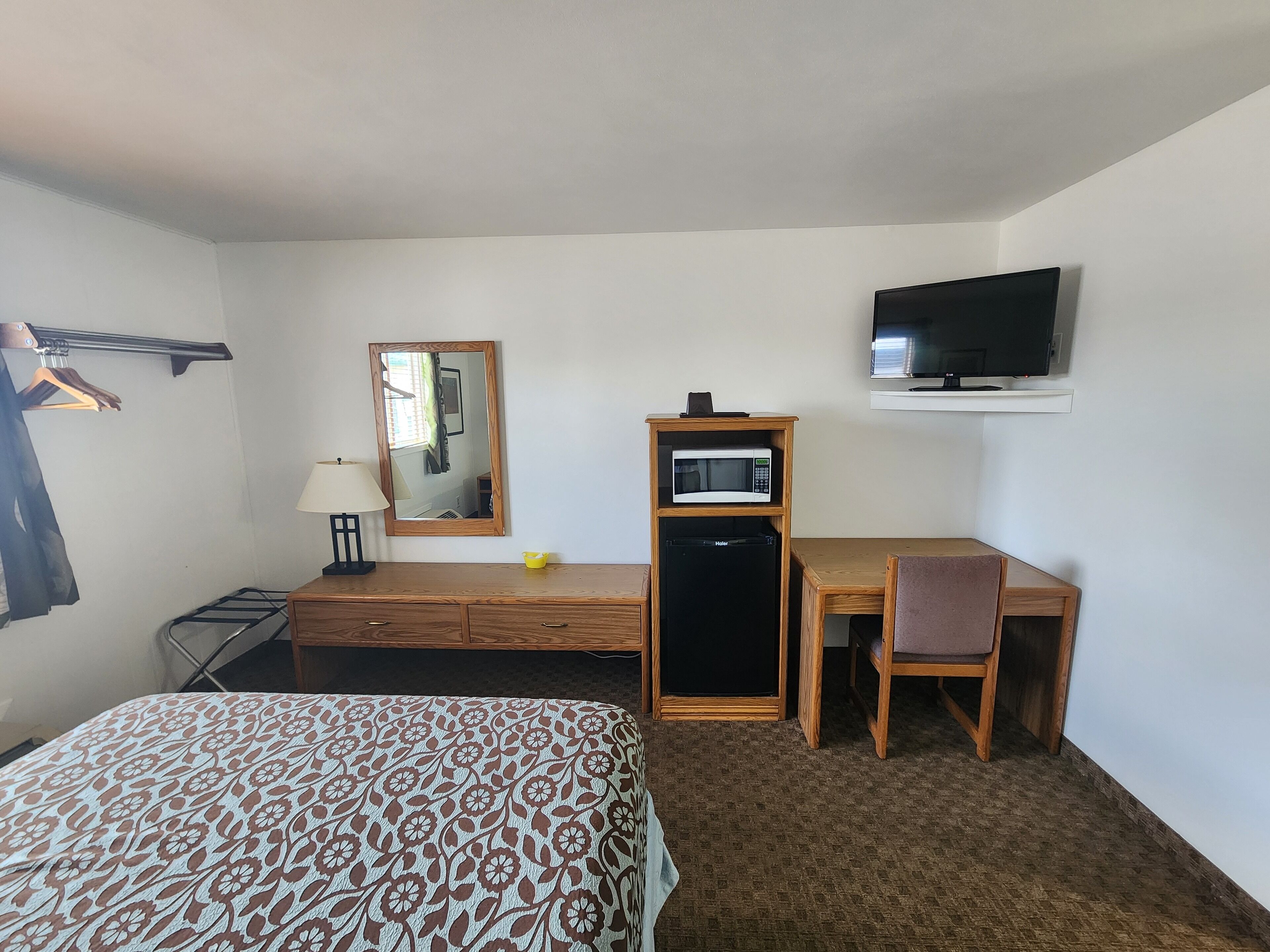 A hotel room with a bed, a desk with a chair, a television, a microwave, and a mirror.