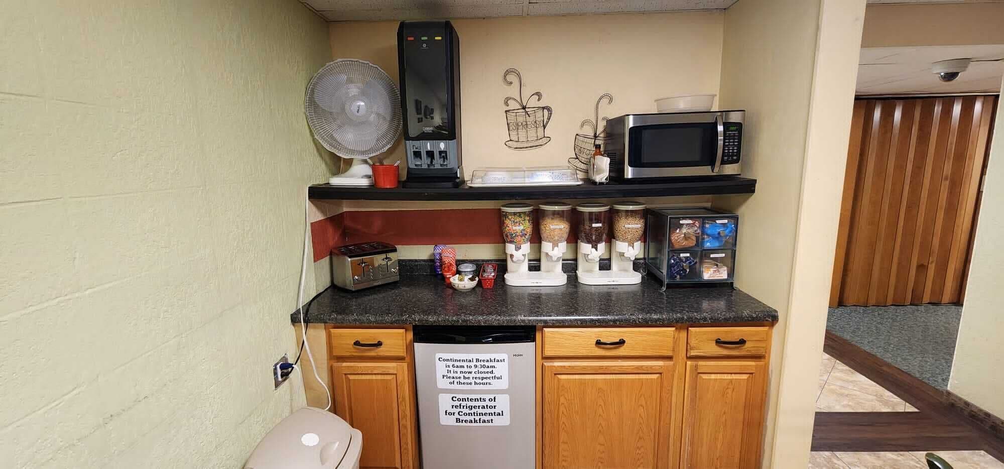 Eine Küchenzeile mit Mikrowelle, Toaster, Kaffeemaschine und einem Schild mit den Frühstückszeiten.