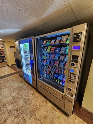 A row of vending machines with snacks and drinks, a payment terminal, and a floor with patterned tiles. - Lantern Motel (Milbank)