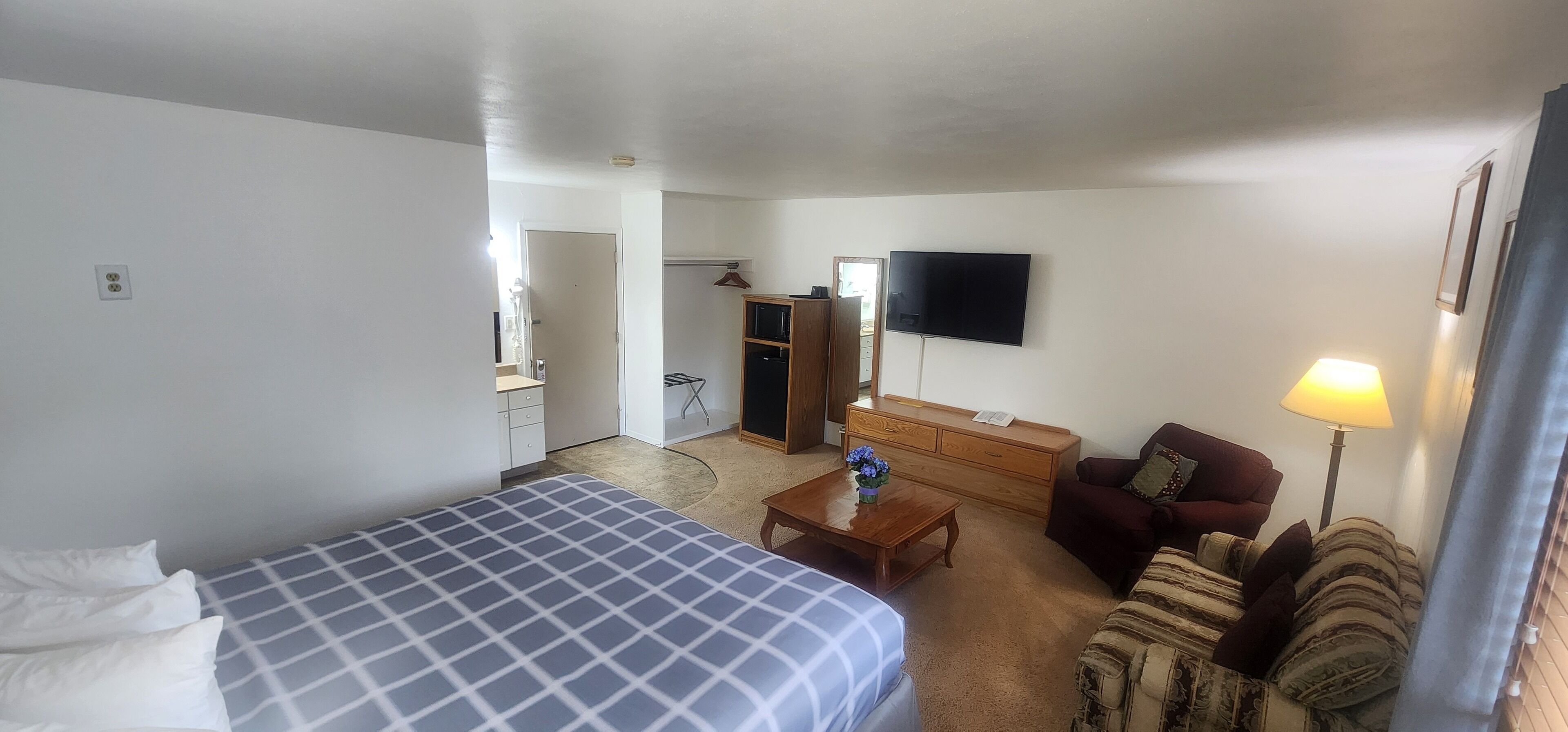A hotel room with a bed, a sofa, a wooden dresser, a TV, and a lamp.