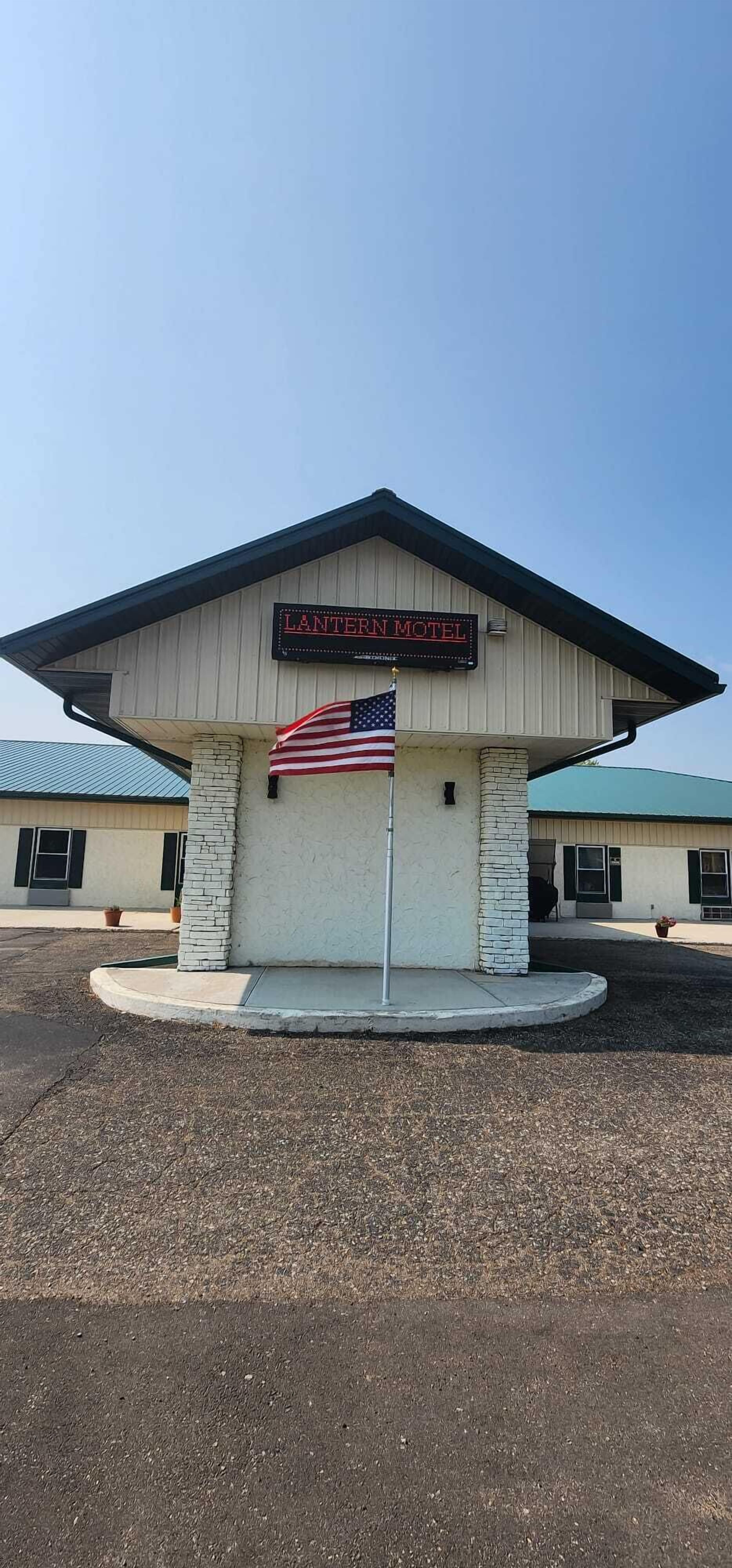 Un motel con un cartel que dice 'Lantern Motel' y una bandera estadounidense al frente.