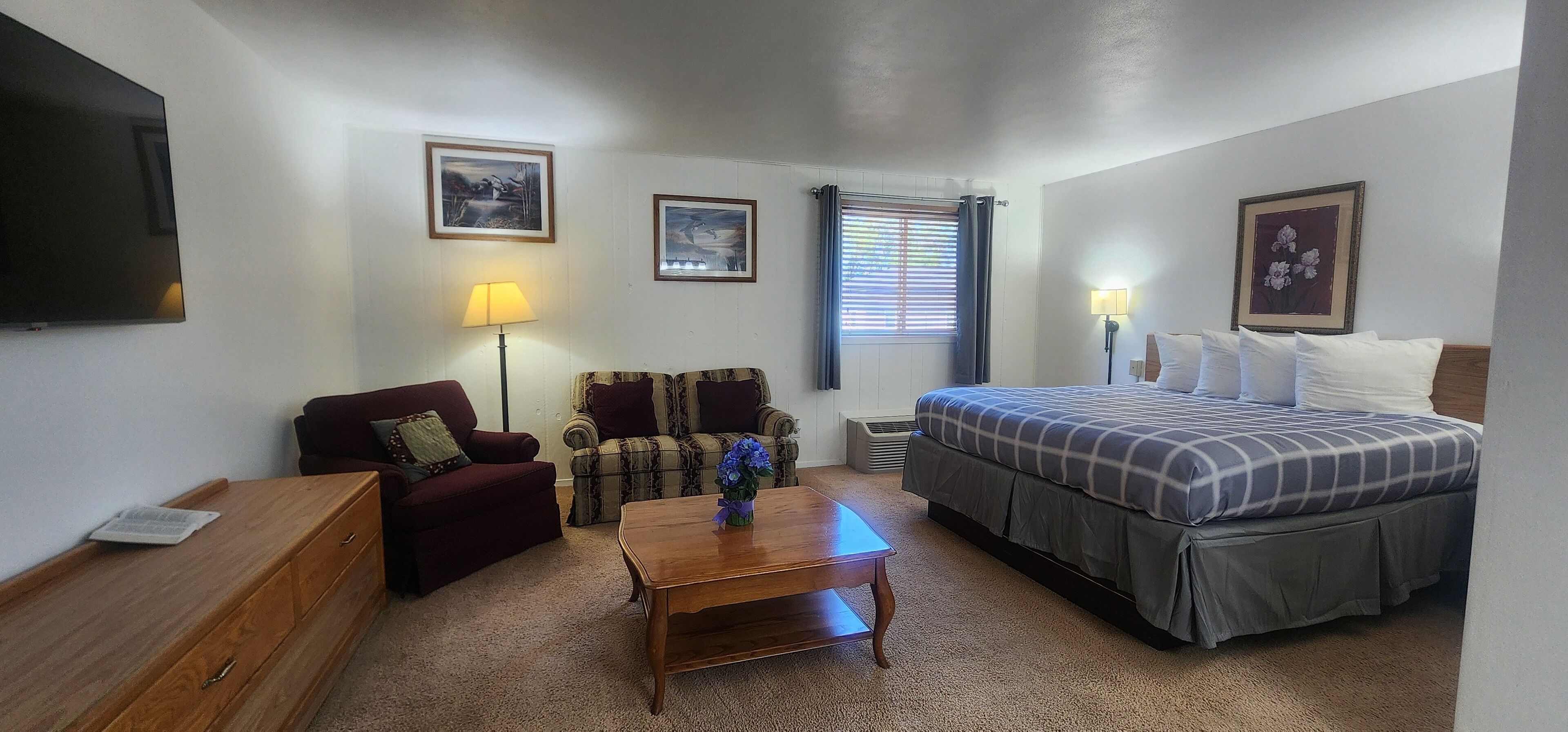 Un dormitorio con cama, sofá, sillón, mesa de madera y televisor en la pared.