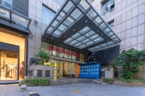A modern building with a glass entrance and a blue door, surrounded by greenery. - Datang City Hotel (Longyan)