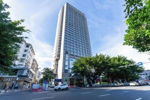 A tall building with a modern design, surrounded by trees and other buildings.