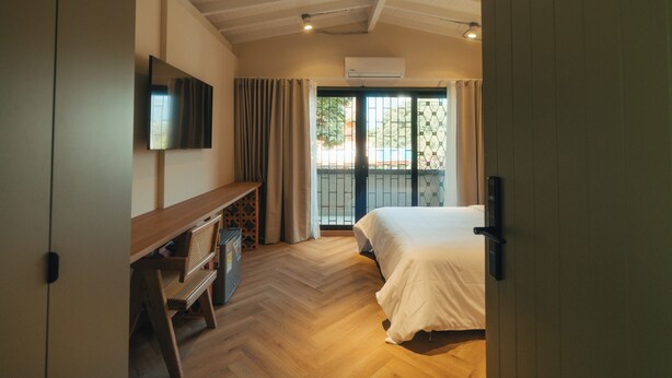 Une chambre à coucher avec un lit, un téléviseur fixé au mur, un bureau avec une chaise et une fenêtre avec des rideaux.