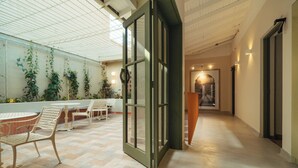 Un vaste espace intérieur doté d’un haut plafond, d’une porte vitrée donnant sur une autre pièce et d’un coin salon avec des tables et des chaises.