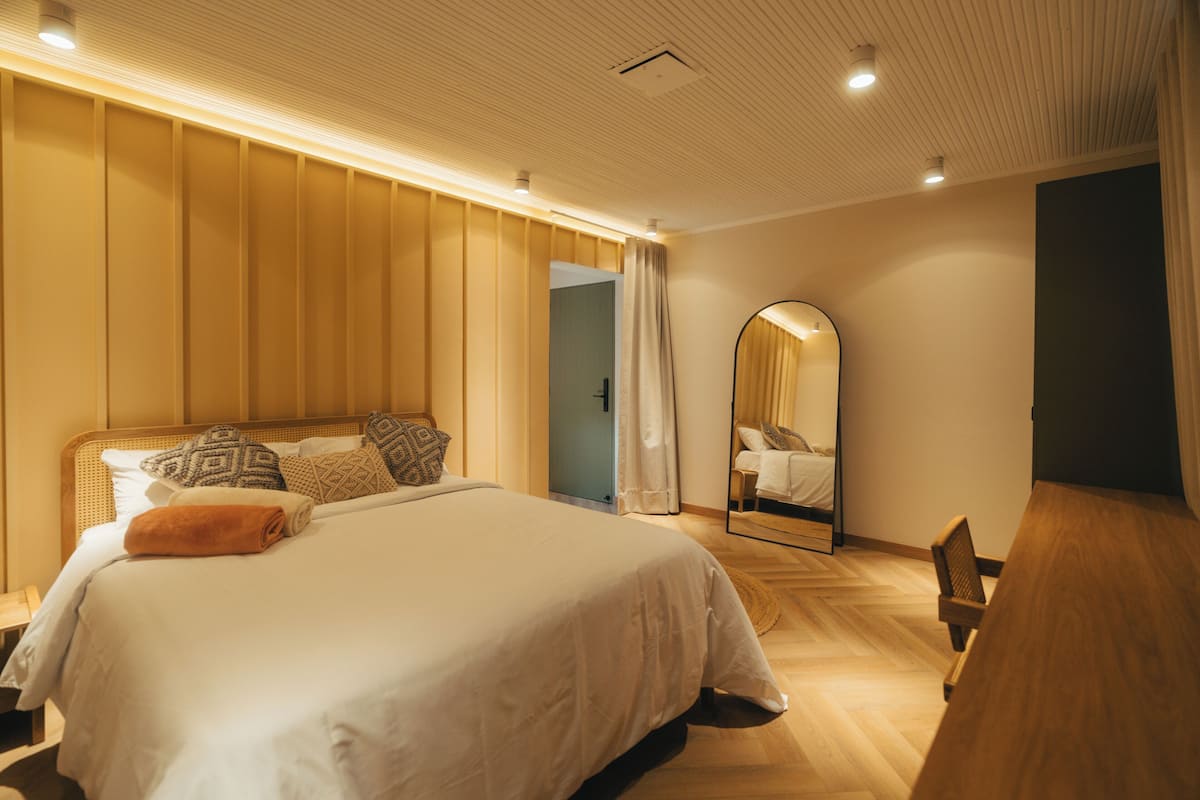 A modern bedroom with a large bed, a wooden desk, and a mirror.
