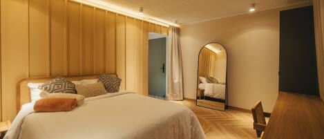 A modern bedroom with a large bed, a wooden desk, and a mirror.