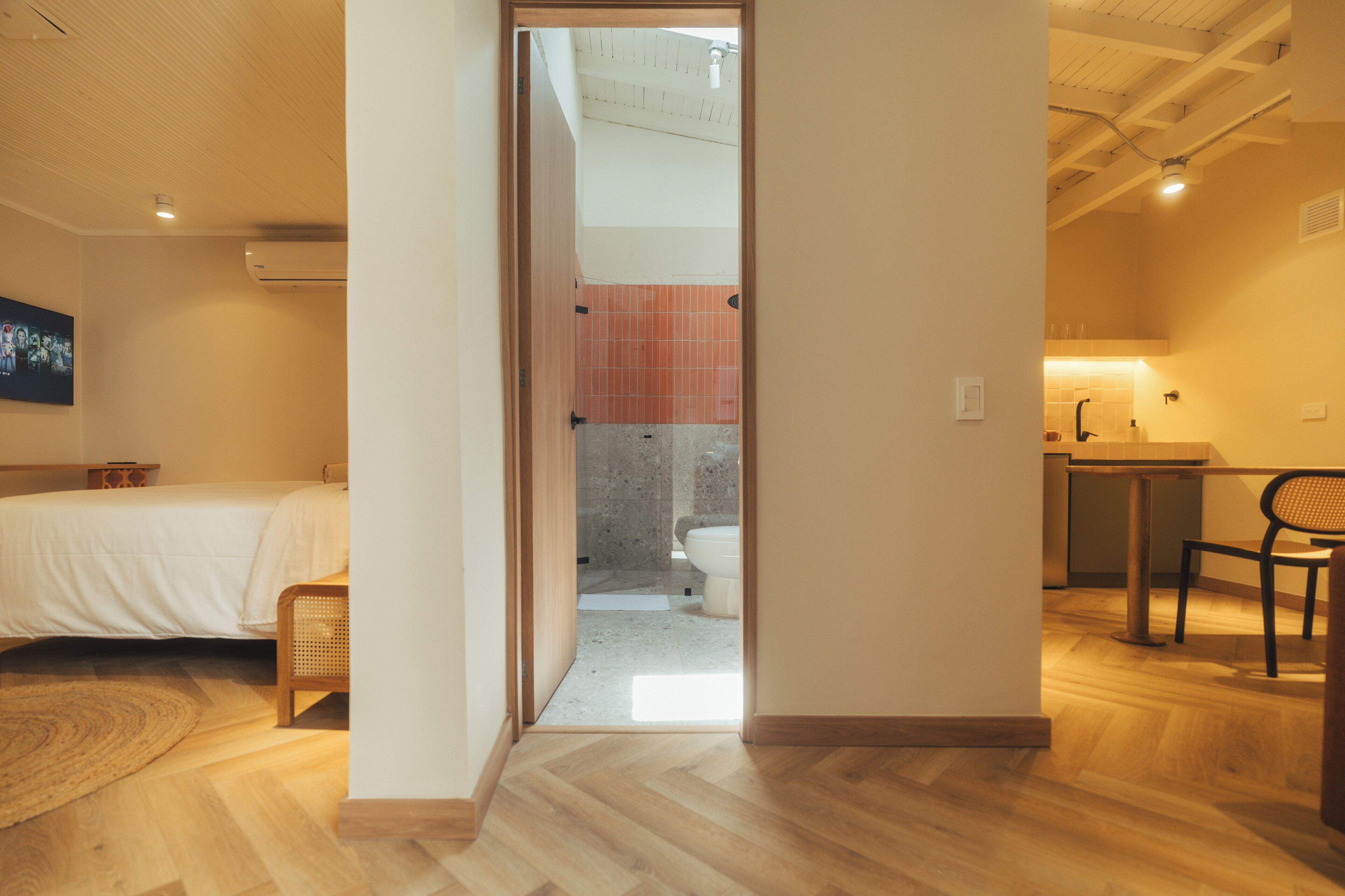 Et moderne hotelværelse med trægulv, seng, lille siddeområde og udsigt til badeværelset.