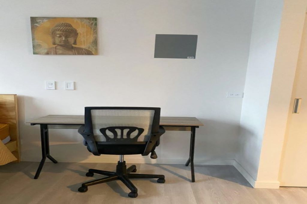 Quarto com escrivaninha, cadeira, pintura de Buda e um pequeno objeto quadrado na parede.