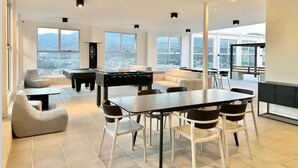 A spacious living area with a dining table, sofas, and a foosball table. Large windows offer a city view. - Beautiful and Cozy Studio in San Jose (San José)