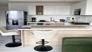 A modern kitchen with white cabinets, a stainless steel refrigerator, a coffee machine, and a dining area with two chairs. - Beautiful and Cozy Studio in San Jose (San José)
