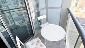 A balcony with a white table and two chairs, large windows, and a view of buildings. - GLOBALSTAY. Charming Lake View 1bd+den in Downtown (Toronto/Canada)