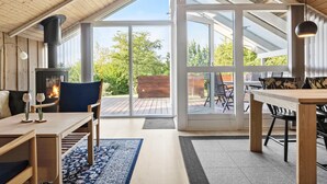 Ein gemütliches Interieur mit Kamin, Holzmöbeln und großen Glasüren, die auf eine Terrasse im Freien führen.