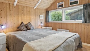 Ein Schlafzimmer mit Holzwandverkleidung, einem großen Bett, zwei Nachttischen und einem Fenster mit Blick auf Grünflächen.