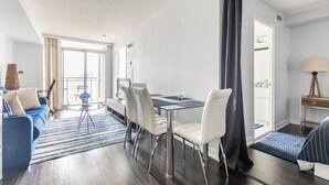Een moderne woonkamer met een blauwe bank, een eettafel met stoelen en een groot raam met gordijnen.